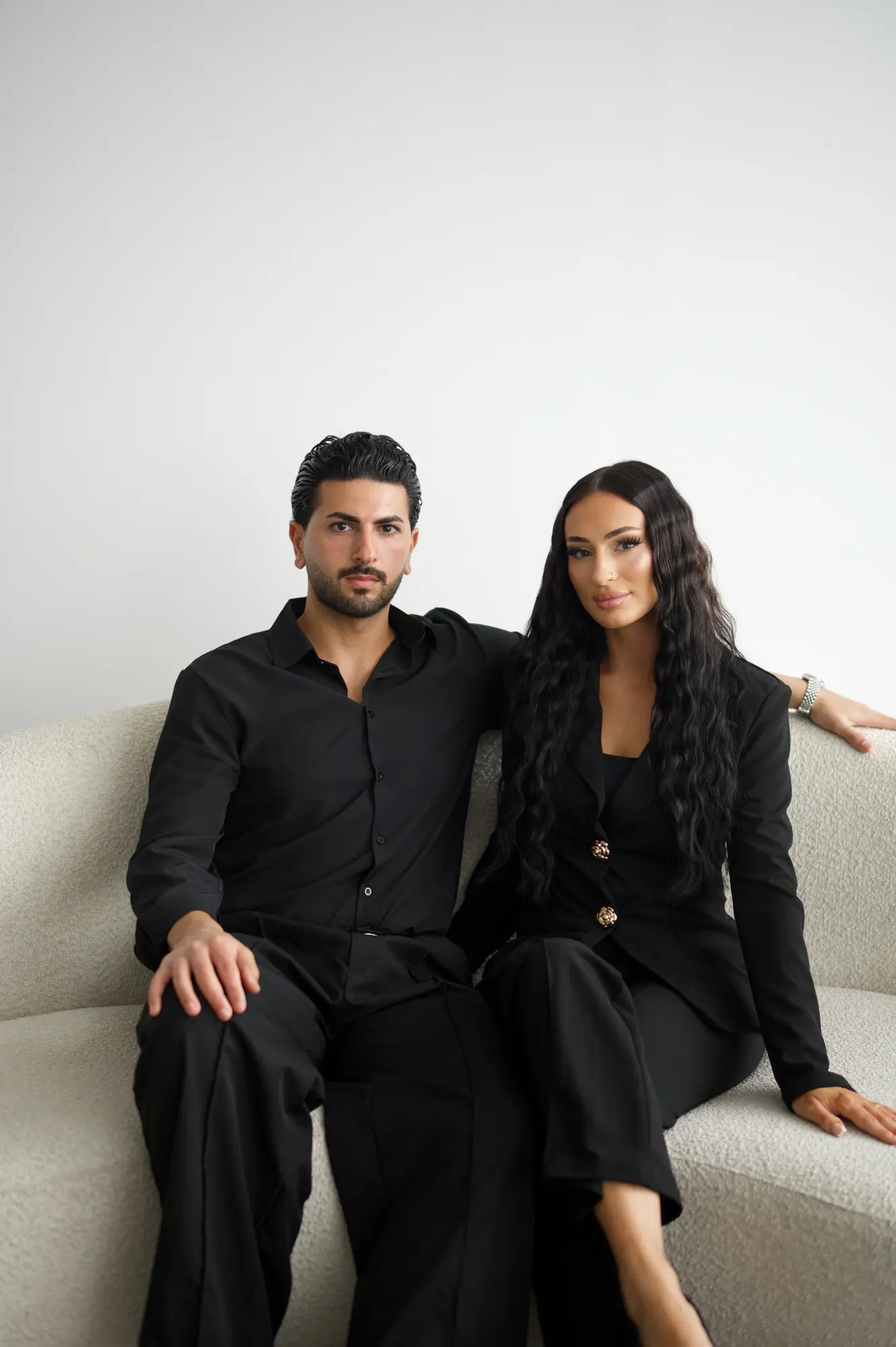 Leyla und Batu, Inhaber von LEYLABEAUTY, in schwarzen Outfits auf einer hellen Couch